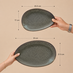 Two views of a dark gray speckled ceramic plate being held by hands, with dimension lines and text showing measurements: 25.5 cm by 17 cm and 33 cm by 21.