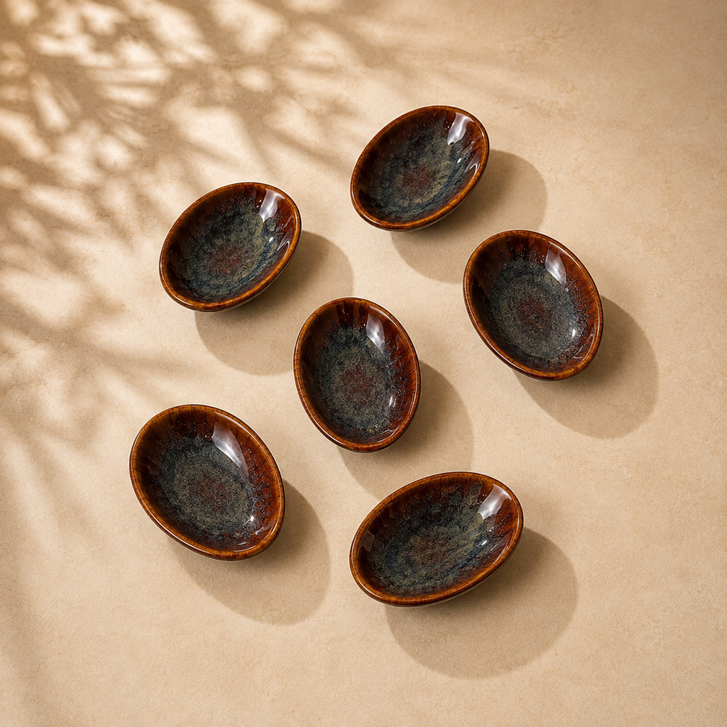 Six Ceramic Amber Tide Petite Server with a glossy dark blue-gray glaze and warm brown rims, arranged on a beige surface with soft leaf shadows.