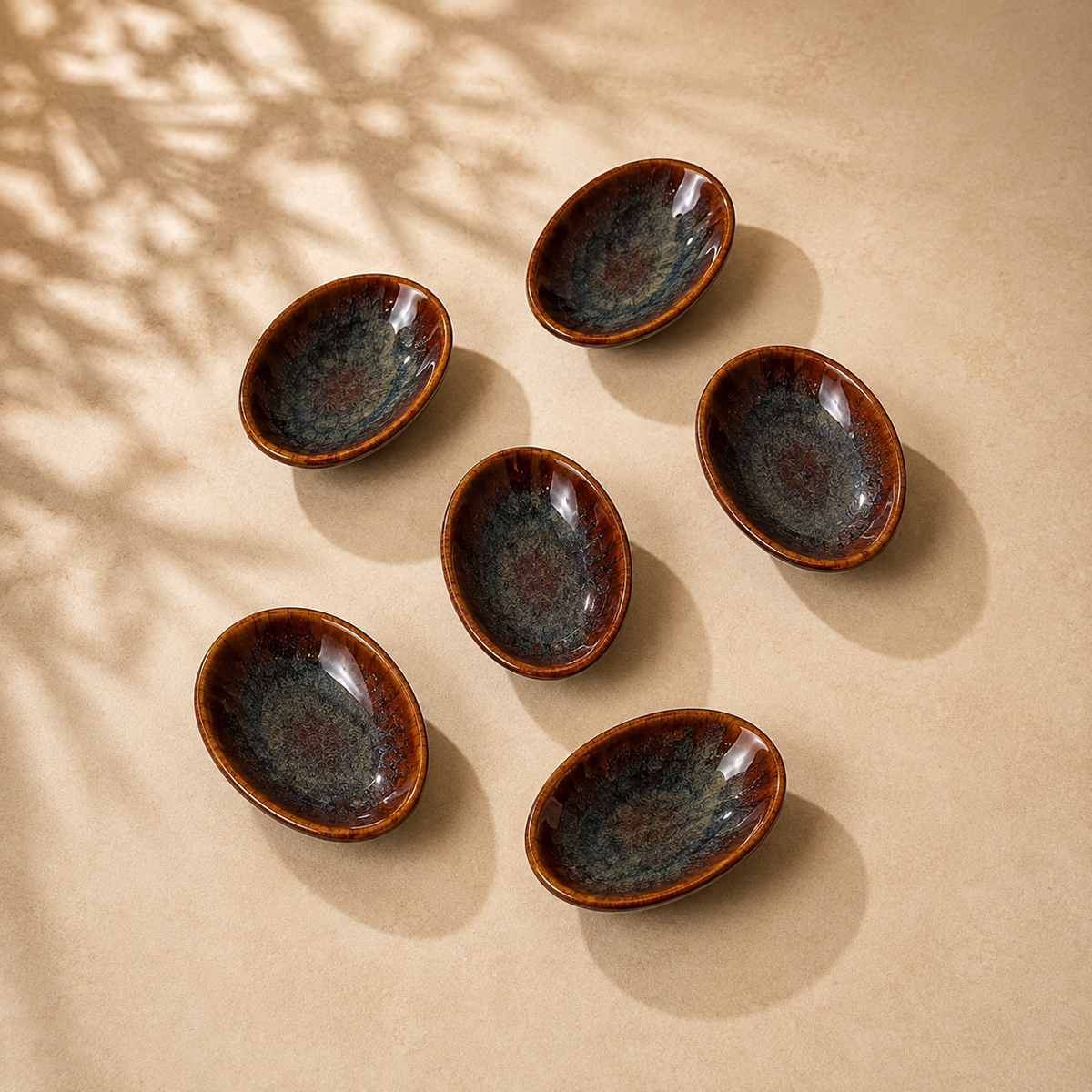 Six Ceramic Amber Tide Petite Server with a glossy dark blue-gray glaze and warm brown rims, arranged on a beige surface with soft leaf shadows.