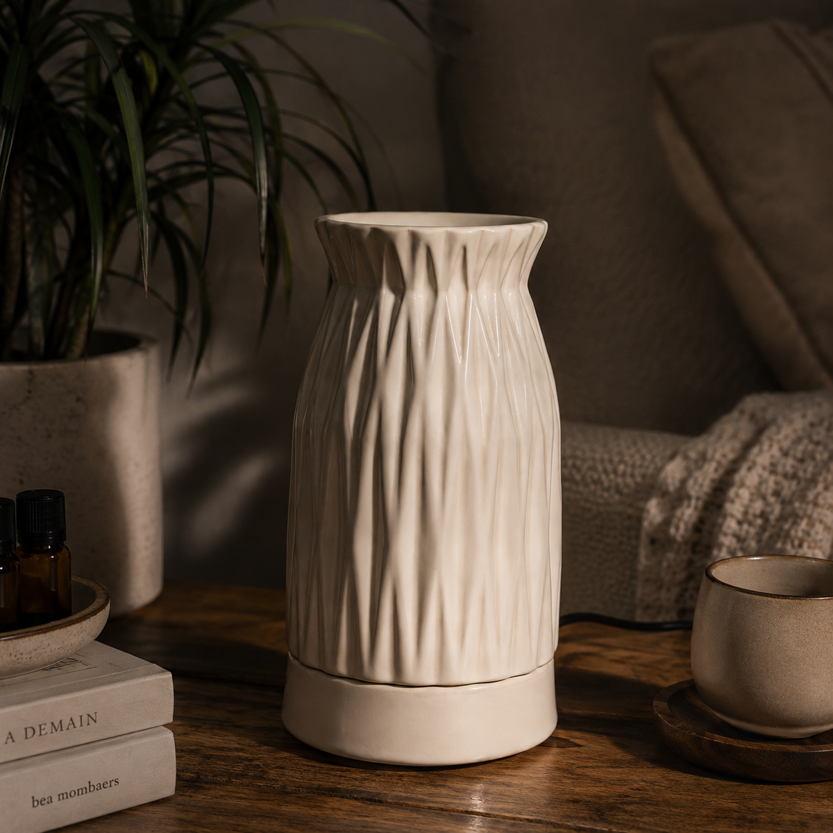 A cream-colored ceramic diffuser with a textured vertical ribbed pattern, sitting on a wooden table in a cozy, dimly lit living room setting.