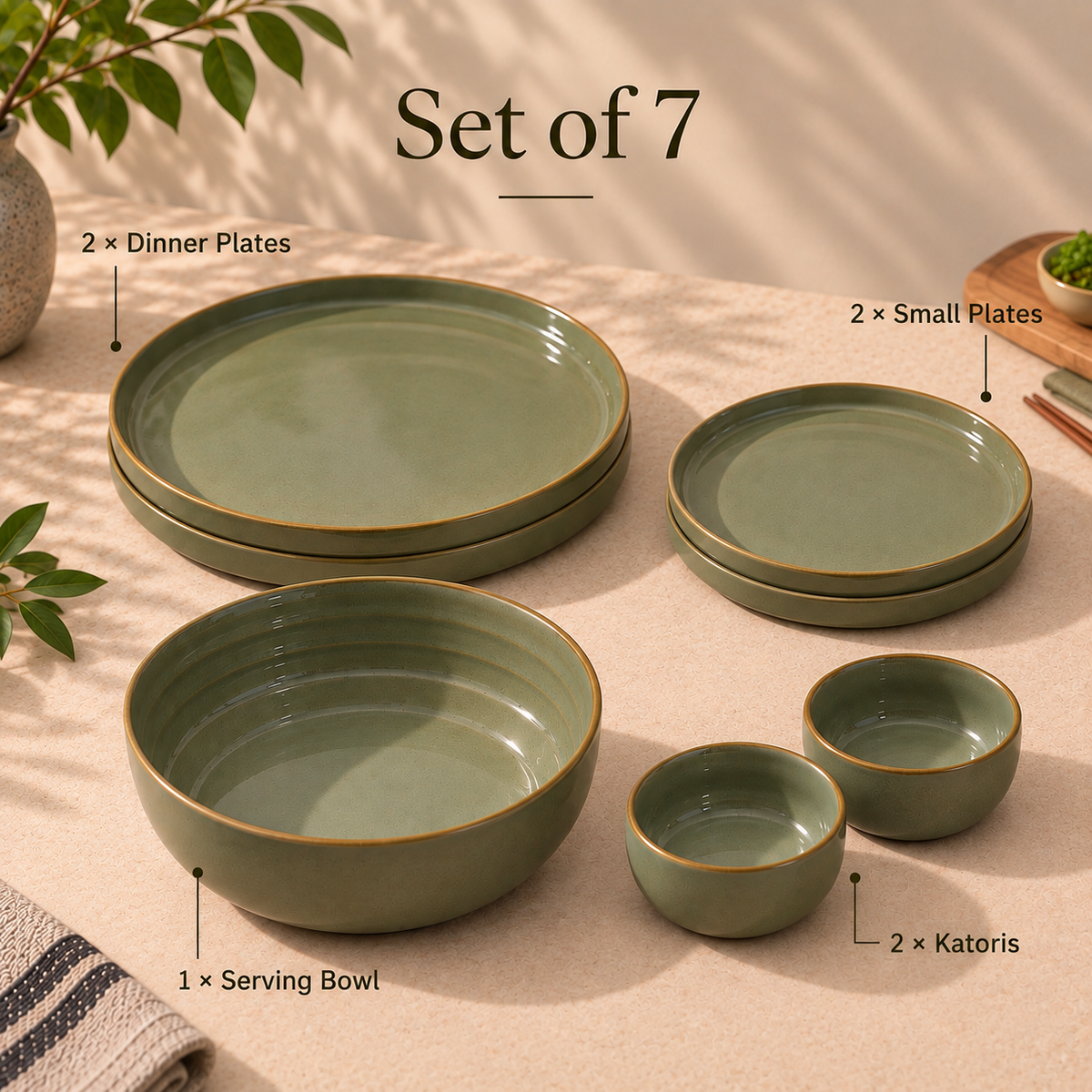 A 7-piece Grove Dinner Set dinnerware set in a muted sage green glaze with gold-toned rims, arranged on a beige tablecloth with text labels identifying each piece: 2 dinner plates, 2 small plates, 1 serving bowl, and 2 katoris. Decorative leaves and a vase appear at the edges.