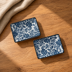 Indigo Bloom dip plate set of two ceramic dishes with a blue floral pattern on a white background, arranged on a wooden tabletop with a beige cloth in the corner.