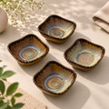 Nest Petite Servers with rounded corners, arranged on a light beige surface. Each bowl has a glossy glaze with concentric circular patterns in blue, yellow, and brown, bordered by a dark speckled rim.