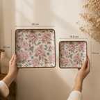 OZAY Living Peony serving platter set  with rounded corners are held by hands against a warm beige wall. The larger tray is 20 cm by 20 cm and the smaller tray is 15.