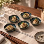 Willow Petite Servers ceramic serving dishes set, each holding a dumpling topped with sesame seeds and green herb garnish, arranged on a beige table runner in a warm dining setting with chopsticks and a bamboo steamer visible.
